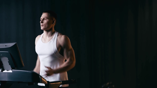 athletic man running on modern treadmill on black  - Metraje, vídeo