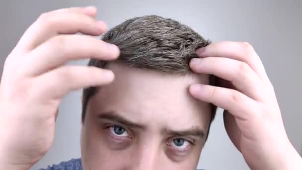 Egy fiatal férfi a tükör előtt vizsgálja a korai ősz haját. A korai hajfehérítés fogalma - Felvétel, videó