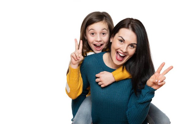 Beautiful young mother and her daughter making peace sign hand gesture, laughing and looking at camera. Isolated over white background. Family love connection concept. - Фото, зображення