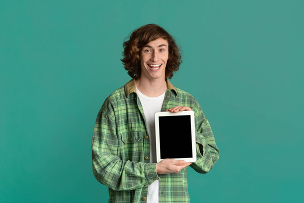 Bonito cara millennial segurando tablet computador com tela em branco no fundo de cor, mockup para o seu projeto
 - Foto, Imagem
