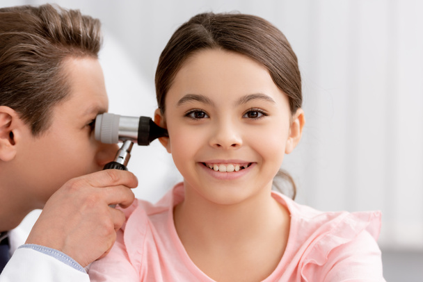 ent physician examining ear of cheerful kid with otoscope - Photo, Image