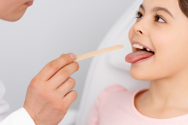 vista recortada del otorrinolaringólogo que sostiene el depresor de la lengua cerca del niño que sobresale de la lengua
  - Foto, Imagen