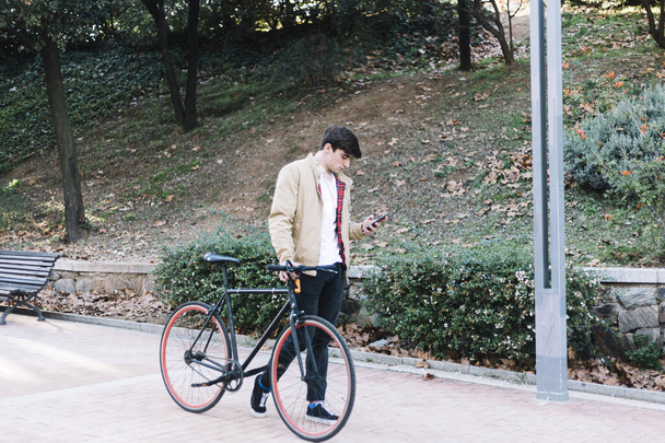 Young man using mobile and carrying a bike while walking outdoors - Foto, imagen
