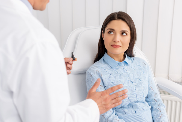 vista recortada del otorrinolaringólogo hablando con un paciente atractivo mientras sostiene el espéculo del oído
 - Foto, imagen