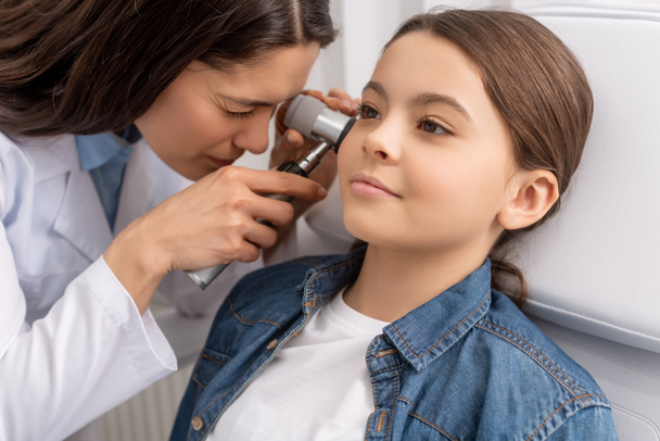 pozorný otolaryngolog zkoumá ucho roztomilého usměvavého dítěte s otoskopem - Fotografie, Obrázek