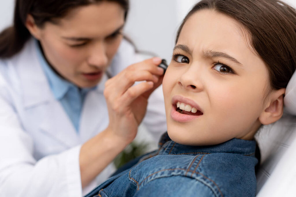 επιλεκτική εστίαση του προσεκτικού ωτορινολαρυγγολόγου εξέταση αυτί του φοβισμένου παιδιού - Φωτογραφία, εικόνα