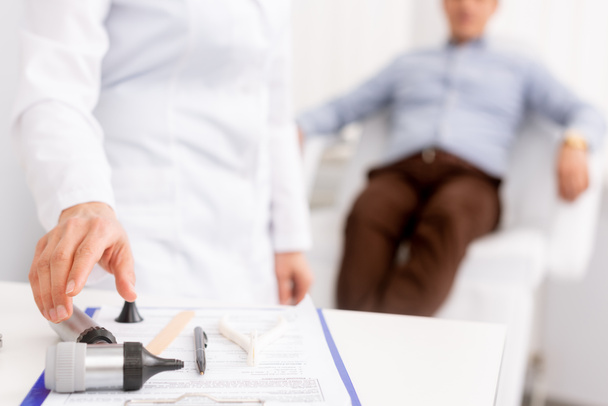 selectieve focus van ent arts die otoscoop en patiënt zitten in een medische stoel op de achtergrond - Foto, afbeelding