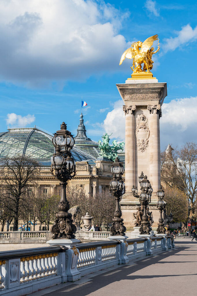 Golden statue and lanterns of Pont Alexandre III bridge with Grand Palais and French flag waving on top of the building - Paris, France - Photo, image