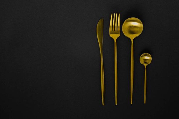 Set of golden instruments - a spoon, fork, knife, teaspoon. Cutlery on a black background - 写真・画像