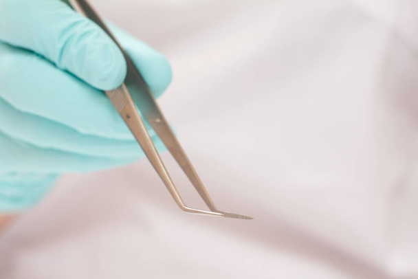 Main de dentiste en gant de latex avec pince à épiler sur fond flou. Concept d'outils médicaux
. - Photo, image