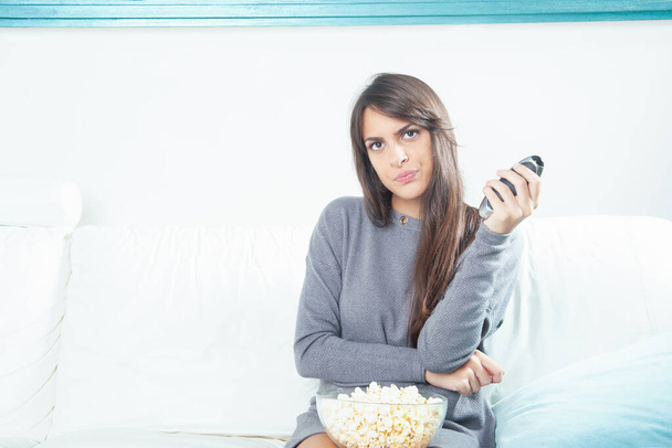 Portrait d'une jeune femme mangeant du pop-corn tout en regardant la télévision à la maison
 - Photo, image