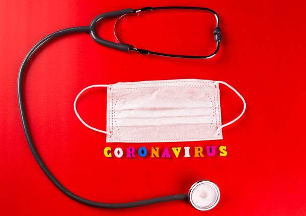 Coronavirus-Wort aus bunten Buchstaben auf rotem Hintergrund. Die Inschrift auf der medizinischen Schutzmaske Coronavirus. - Foto, Bild