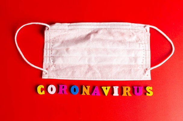 Palabra de Coronavirus hecha de letras de colores sobre fondo rojo. La inscripción en la máscara protectora médica coronavirus
. - Foto, Imagen
