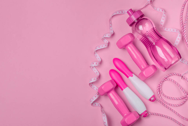 Dumbbells, bottle of water, jump rope and measuring tape on pink background - Foto, imagen