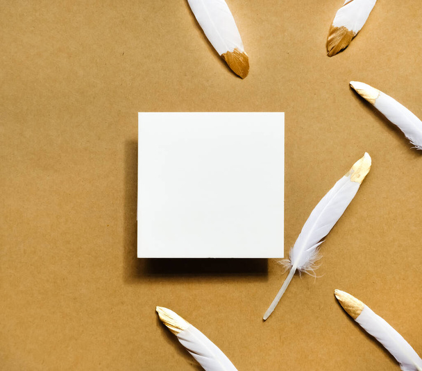 White square card and feathers on brown paper background. Festive minimal concept.  - 写真・画像