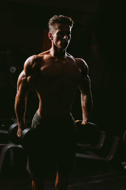 muscular man with weights in gym. Bodybuilder handsome male. Torso. silhouette shot. - Foto, afbeelding