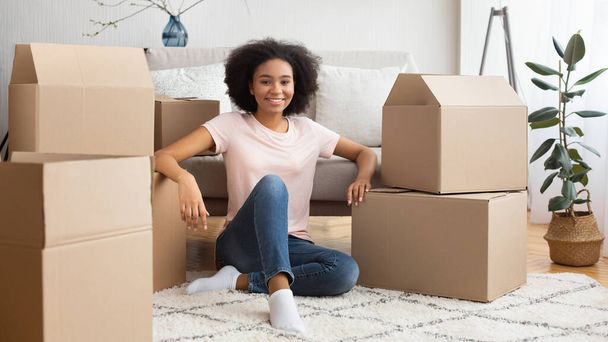 Smiling african american girl sitting on floor surrounded by a lot of boxes - Fotó, kép