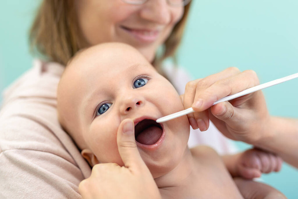 Médico pediatra examinando la garganta y los dientes de los niños. Mamá sosteniendo al bebé con las manos mientras chequea la salud. Medicina, salud, pediatría y personas. Concepto de salud y prevención de enfermedades infantil
. - Foto, Imagen