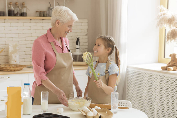 Adorable petite fille aidant sa grand-mère à cuisiner dans la cuisine, espace vide
 - Photo, image