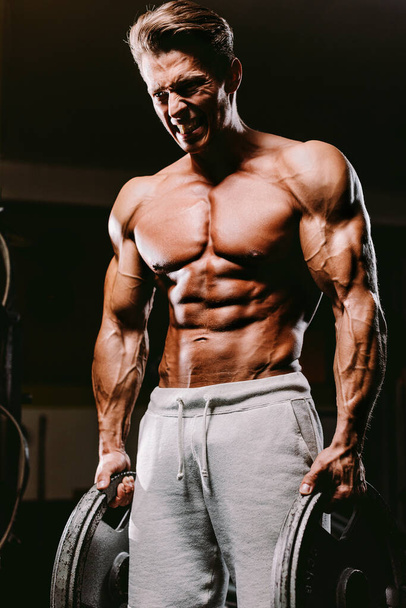 Muscular fit man pumping muscles. Bodybuilder showing strength. Hard workout in gym. - Photo, Image