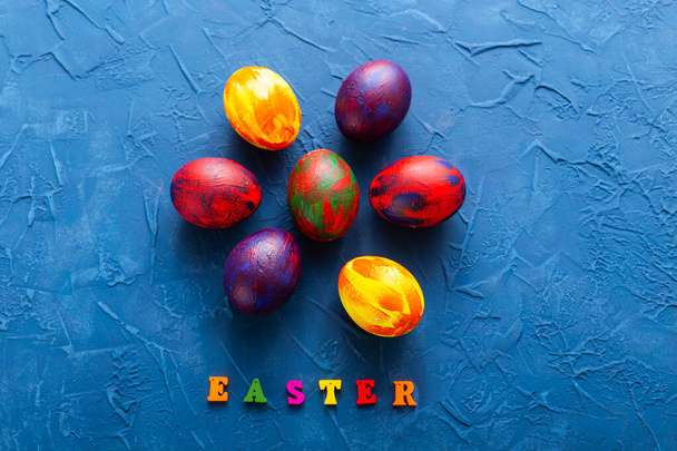 Multi-colored wooden letters making up the words happy easter and decorative colourful eggs on a blue background. Top view. - Photo, Image