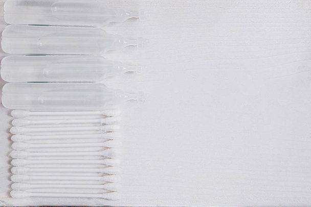 A row of ampoules and cotton swabs on a white background. Space for text. The concept of viral infection. - Photo, Image