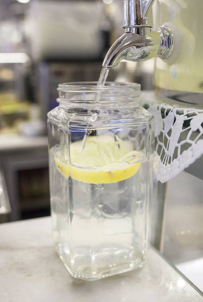 Dávkovač limonád naplňuje velkou sklenici plátkem citronu. Kávovnu pozadí - Fotografie, Obrázek