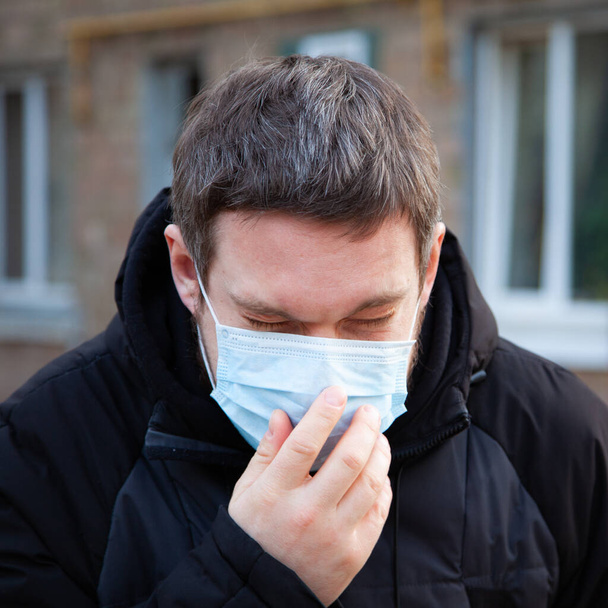 Virüs covid-19. Tıbbi maskeli bir adam Avrupa 'da bir şehirde hapşırır ve öksürür. Koronavirüsten korur. - Fotoğraf, Görsel