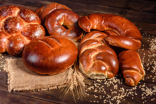Σύνθεση φρέσκου ψημένου γλυκού ψωμιού με παπαρούνα και μαρμελάδα. Γλυκό ψήσιμο απλωμένο ως σύνθεση σε ξύλινο τραπέζι - Φωτογραφία, εικόνα