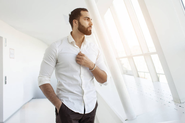 Porträt eines erfolgreichen gutaussehenden Mannes in weißem Hemd am Morgen in einem weißen Gebäude, Geschäftsmann blickt aus dem Fenster, Kopierraum - Foto, Bild