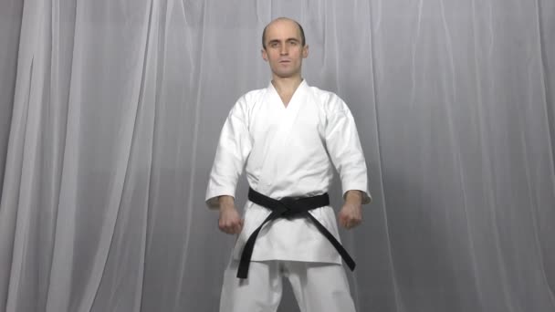 Adult athlete trains karate formal exercises on a light background - Footage, Video