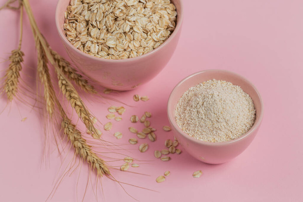 Bowl of dry oat flakes with oatmeal and ears of wheat on light background. Healthy skin, facial and body care. SPA and sauna concept. - Photo, image