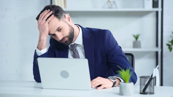 Ofiste dizüstü bilgisayarın yanında oturan takım elbiseli üzgün iş adamı  - Video, Çekim