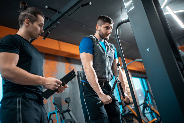 young man has workout with personal trainer in modern gym - Foto, Bild