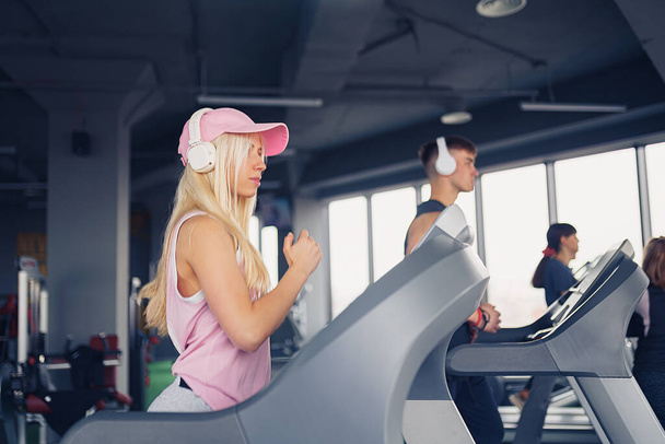 Music and exercises go together. Couple working exercise on treadmill. Focus is on woman - Foto, Imagen