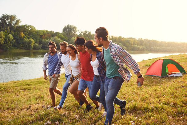 Friends have fun running along the lake on a picnic. - Foto, afbeelding