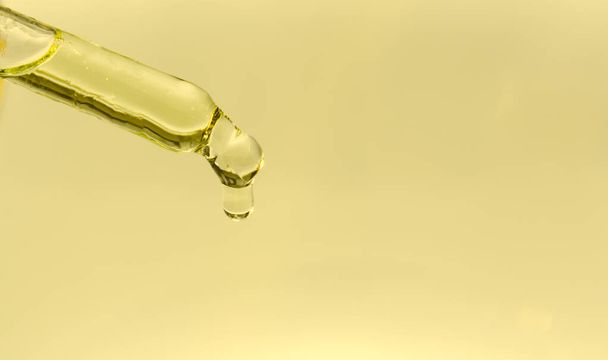 Op een gele achtergrond een glazen pipet met cannabis olie. Een druppel druppels van het uiteinde van de pipet. Concept - illegaal drugsgebruik. Kopieerruimte - Foto, afbeelding