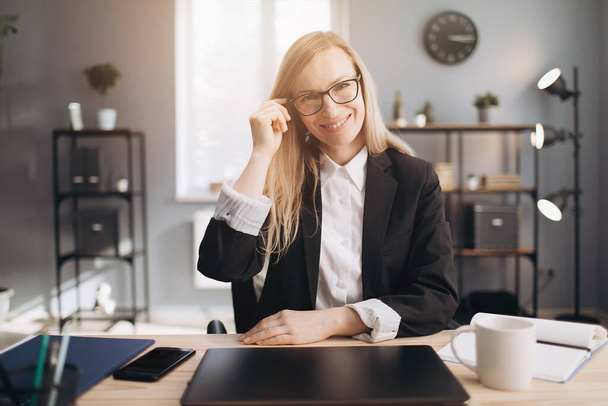 Smiling woman in eyeglasses sitting at modern office - Foto, afbeelding