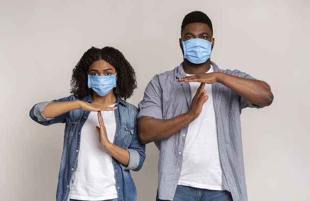 Nuori musta pari suojaavissa lääketieteellisissä naamioissa, jotka näyttävät aikalisän eleen
 - Valokuva, kuva
