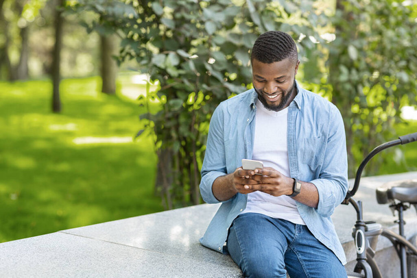 Fekete Hipster Guy használ okostelefon a szabadban, ül a padon a parkban - Fotó, kép
