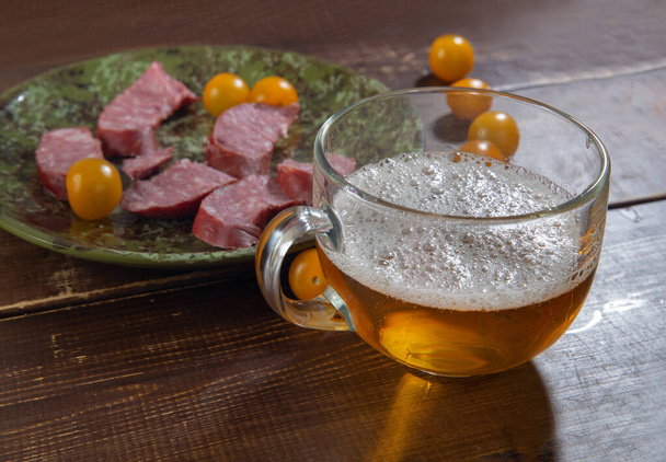 Glass of beer and polish sausage and yellow cherry tomatoes  on brown table  - Фото, зображення