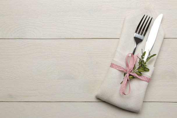 Configuración de la mesa. Cubertería en una servilleta blanca con una cinta rosa, tenedor y cuchillo en una mesa de madera blanca. vista superior
 - Foto, imagen