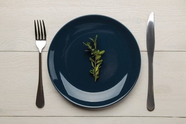 Ρύθμιση τραπεζιού. Μπλε πιάτο και μαχαιροπήρουνα, πιρούνι και μαχαίρι σε λευκό ξύλινο τραπέζι. πάνω όψη - Φωτογραφία, εικόνα