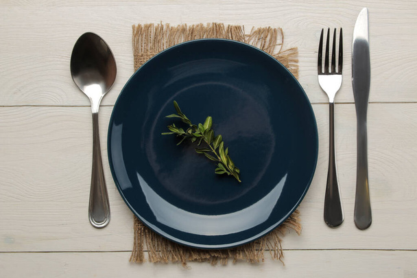 Apparecchiare. Piatto e posate blu, forchetta, cucchiaio e coltello su un tavolo di legno bianco. vista dall'alto
 - Foto, immagini