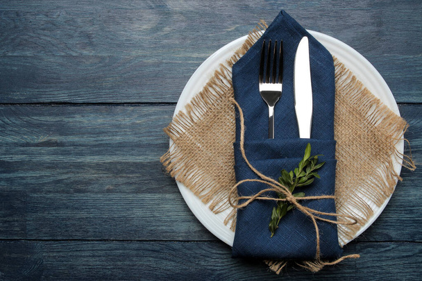 Tafelopstelling. bord en bestek in een blauw servet, vork en mes op een blauwe houten tafel. bovenaanzicht - Foto, afbeelding
