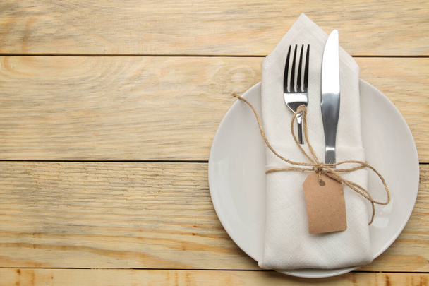 Tafelopstelling. Bord en bestek in een witte servetvork en mes op een natuurlijke houten tafel. bovenaanzicht - Foto, afbeelding