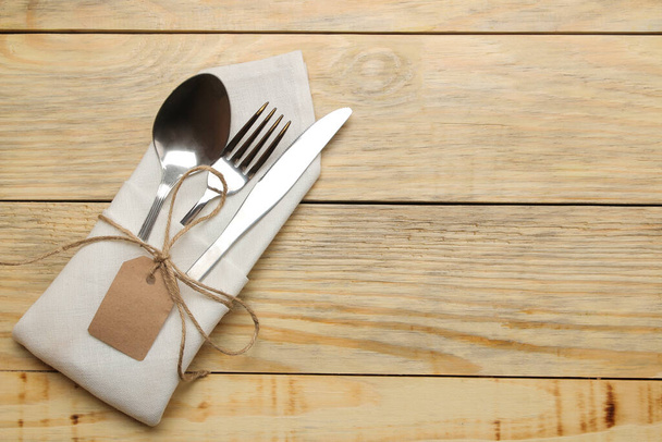 Configuración de la mesa. Cubertería en una servilleta blanca, tenedor, cuchara y cuchillo en una mesa de madera natural. vista superior
 - Foto, imagen