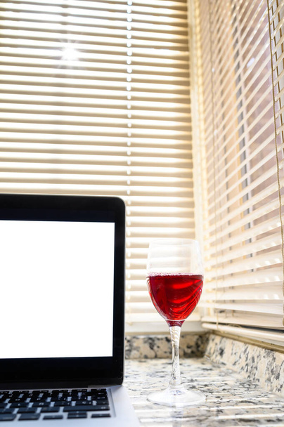 Szklankę czerwonego wina i laptopa z białym ekranem. Pionowa przestrzeń do kopiowania.Relaks w domu koncepcja. - Zdjęcie, obraz