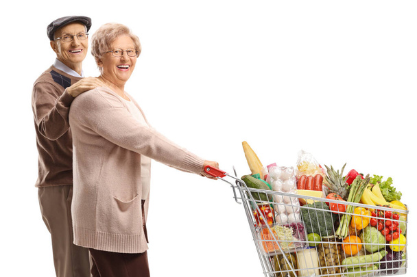 Marido y esposa mayores caminando y empujando un carrito de compras con alimentos aislados sobre fondo blanco
 - Foto, imagen
