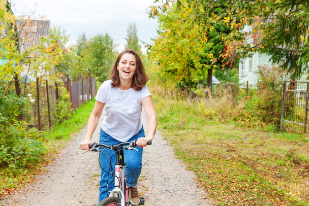 Молода жінка їде на велосипеді в літньому міському парку на відкритому повітрі. Активні люди. Хіпстерська дівчина розслабляється і їде на велосипеді. Велоспорт на роботу в літній день. Концепція велосипедного та екологічного способу життя
 - Фото, зображення